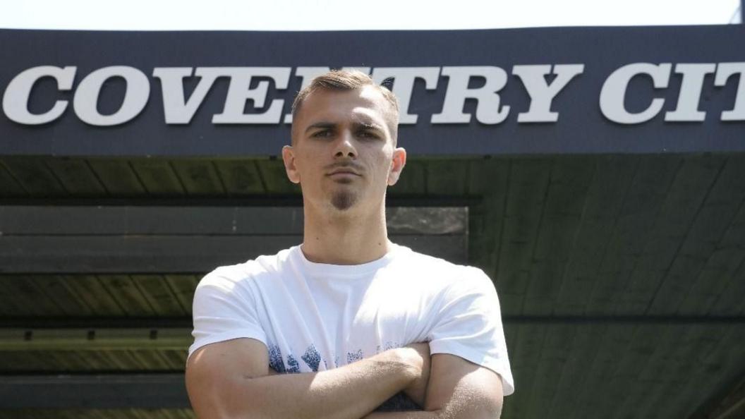 New Coventry City signing Miguel Ángel Brau posed with his arms crossed in front of the stand at the CBS Arena that shows Coventry City on its roof