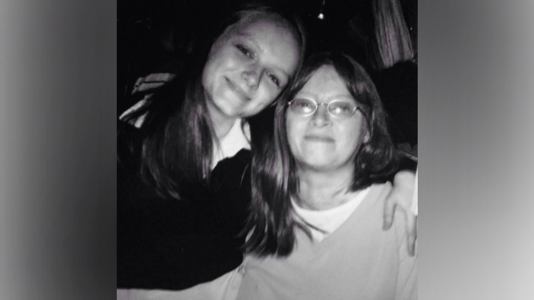 A young girl smiles as she hugs her mother.