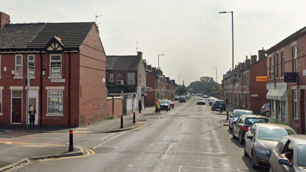 Google streetview of Lloyd Street junction with redbrick terraced houses on both sides. Cars are parked on the right with bollards on the left.