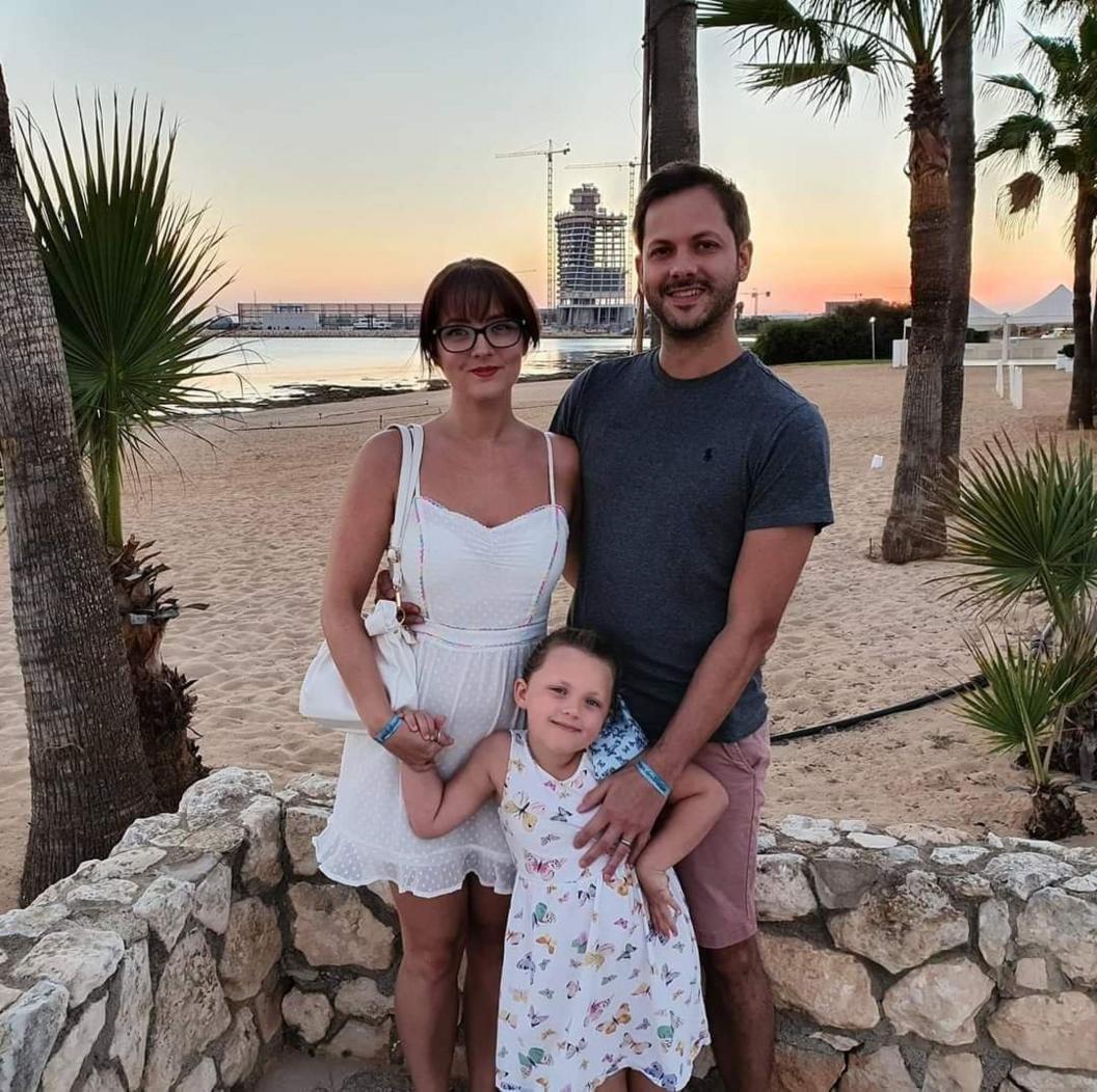 A couple and their 4 year old daughter pose for a holiday picture near a beach in Cyprus