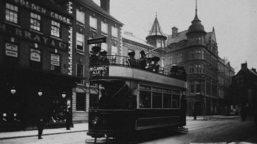 A black and white scene of a city street with an old-fashioned tram driving down the middle of the road.