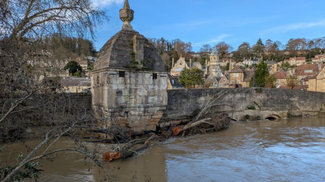 Town Bridge with floodwater right up to road level and a large tree trunk stuck at the parapet