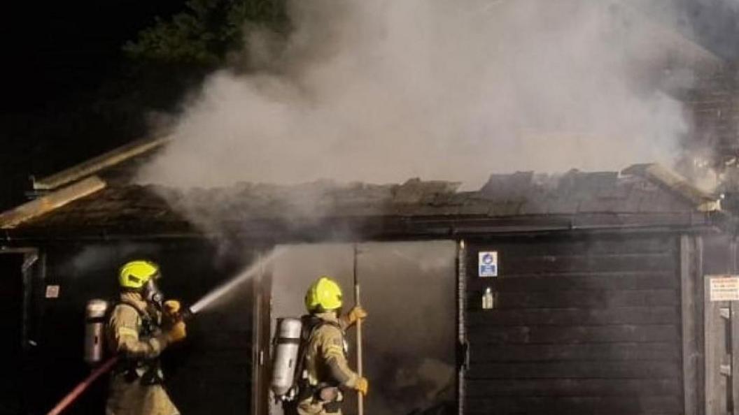 Firefighters spray water on a building, which has smoke pouring from it