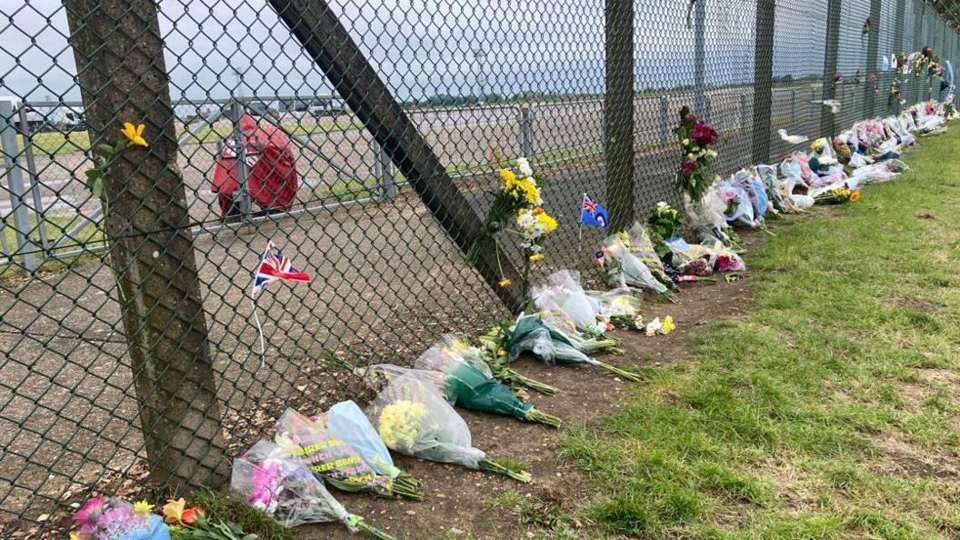 Bouquets of flowers placed again a mesh wire perimeter fence at RAF Coningsby