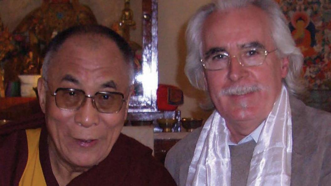 The Dalai Lama is on the left and is wearing glasses and a robe. Charlie has longish white hair and glasses. He is wearing a white silk scarf.