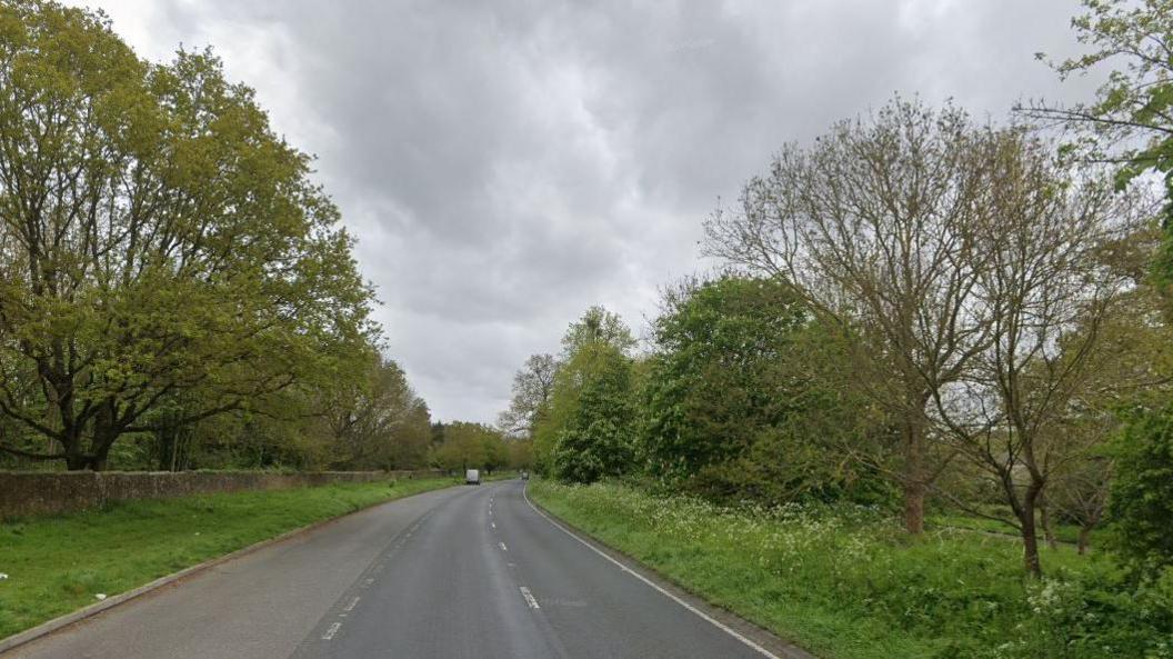 The A414, with three lanes and trees on both sides of the road