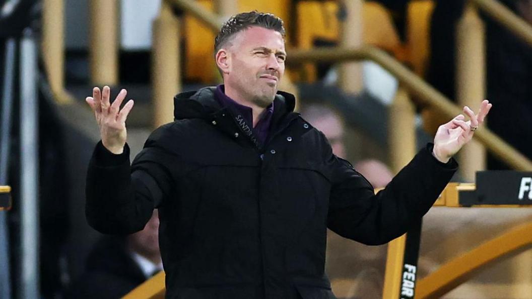 Rob Edwards, wearing an all-black outfit in the dugout at Molineux, reacting to Wolves' game against Brentford in December