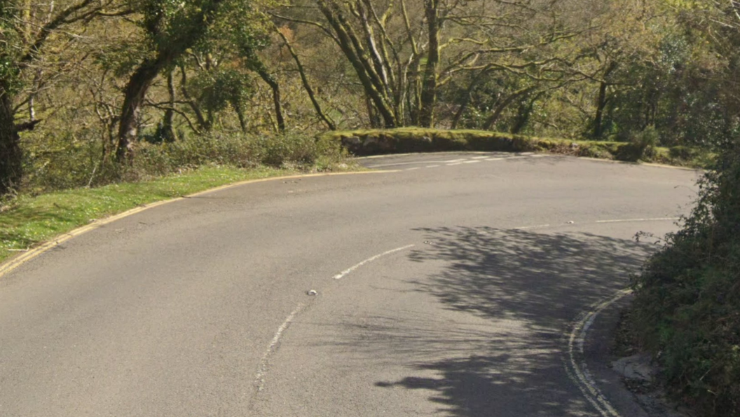 The sharp bend at the Spitchwick junction is lined with an old stone wall covered in moss and lined with trees.