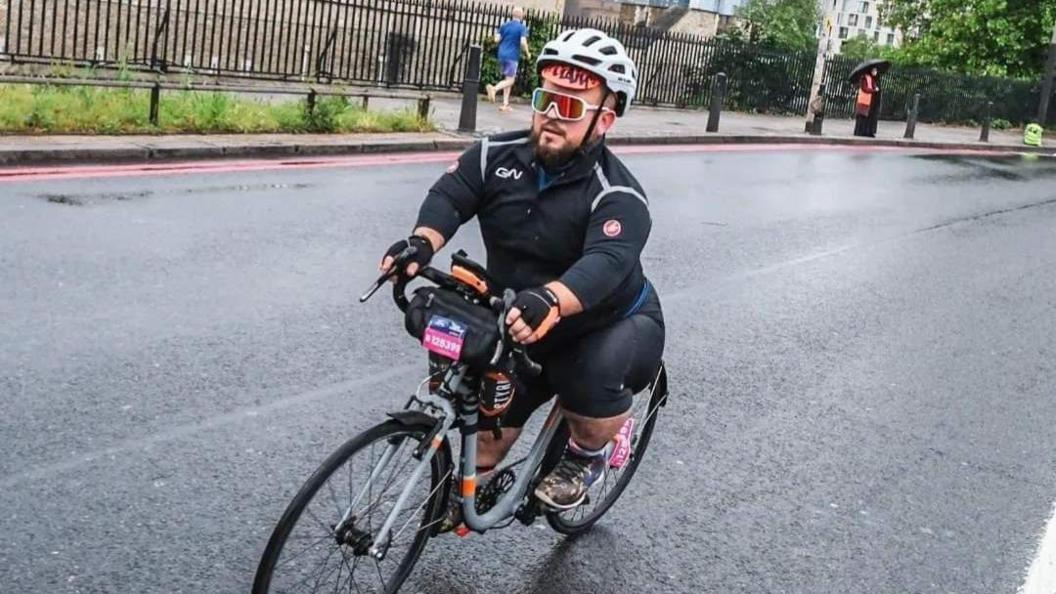 A man with achondroplasia on a bike on the road with a helmet and reflective glasses on.