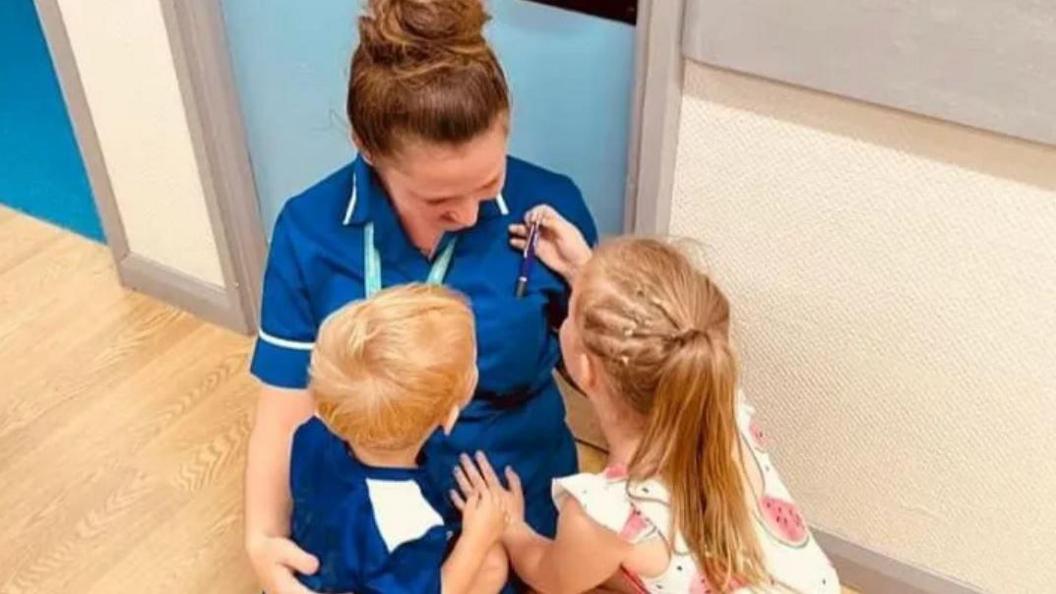 Woman dressed in blue tunic crouched down with two children