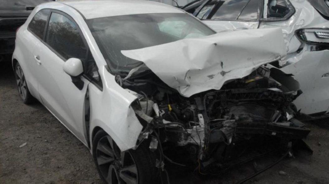 a white Kia Rio car with extensive damage to its hood and bumper, which are crumpled