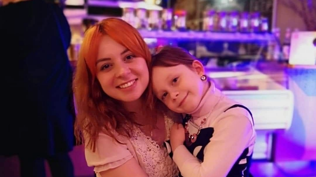 A woman with dyed orange hair smiles for the camera with a a young girl sitting on her lap, also smiling for the camera.