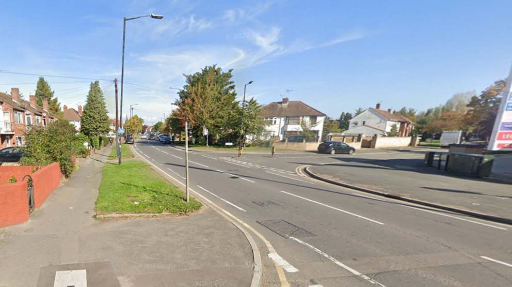 A Google Maps picture of Stoke Poges Lane. It is a residential road, with a petrol station on the right of the picture. There are semi-detached houses with small front gardens in front of the properties along the road.