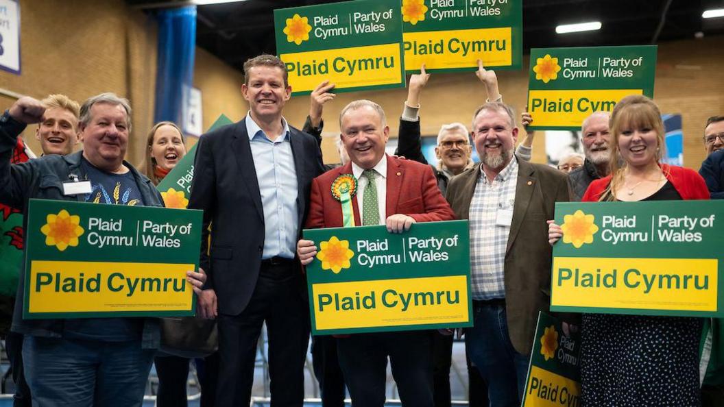 Plaid Cymru members holding green and yellow placard