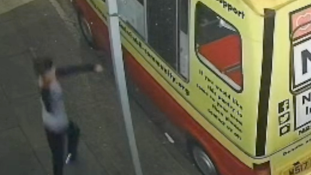 A screenshot of CCTV footage of a child throwing something at the van. One side window is already broken. The child appears to be wearing black jogging bottoms and a grey and black sports top. He has short dark hair.