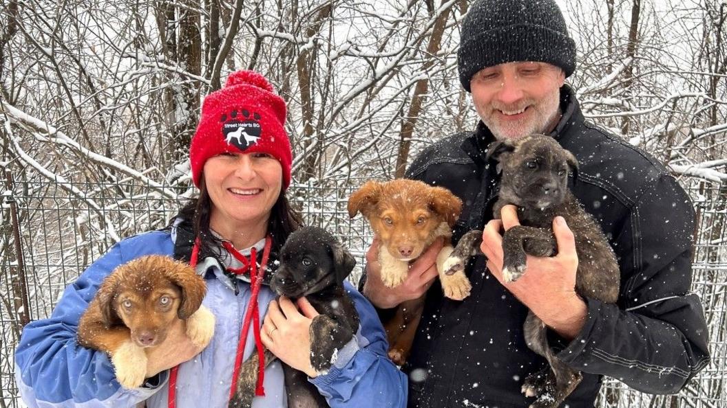 Emma and Anthony in the snow holding four dogs