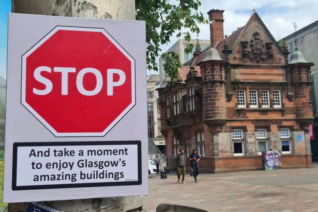 A photo of the former St Enoch station in the centre of Glasgow and a sign which says STOP - and take a moment to enjoy Glasgow's amazing buildings