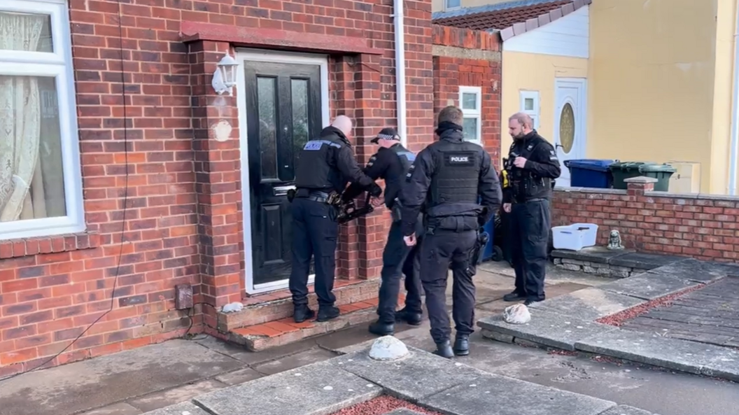 Police atempting to break down a door during a drugs raid as part of Operation Artemis