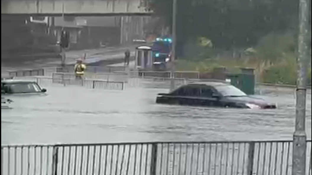 Two cars submerged in water off the roundabout. A fire engine can be seen in the background with a fire officer standing in the water.