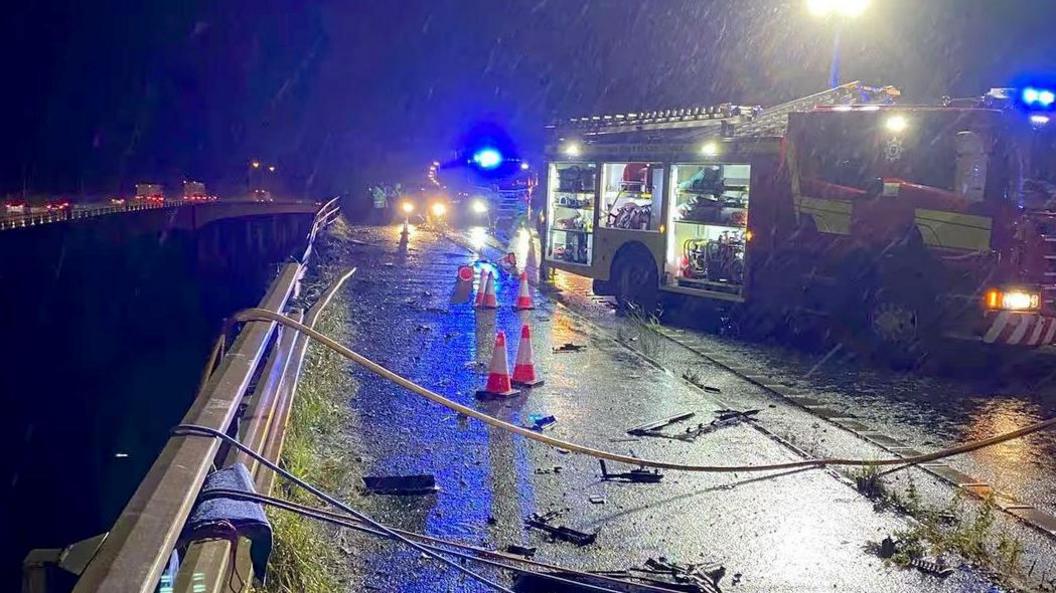 A fire engine with its lights on in the driving rain on the M6 above the crash site