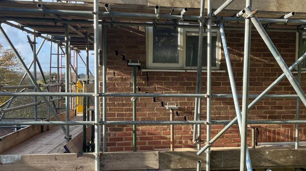 Scaffolding around a house. Cracks in the brickwork running down the side of the wall are visible