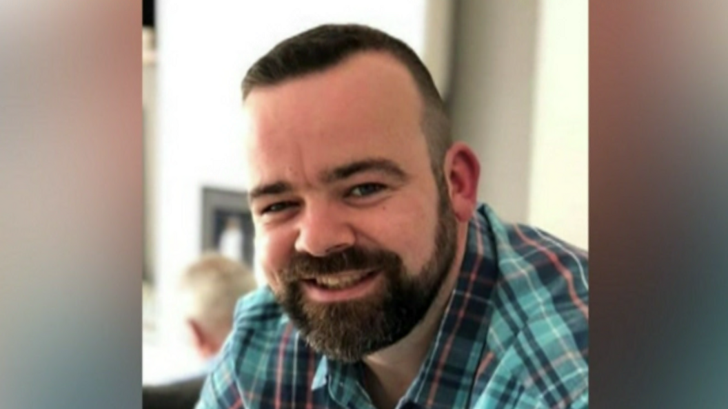 Man with dark hair and beard, with a flannel shirt on. 