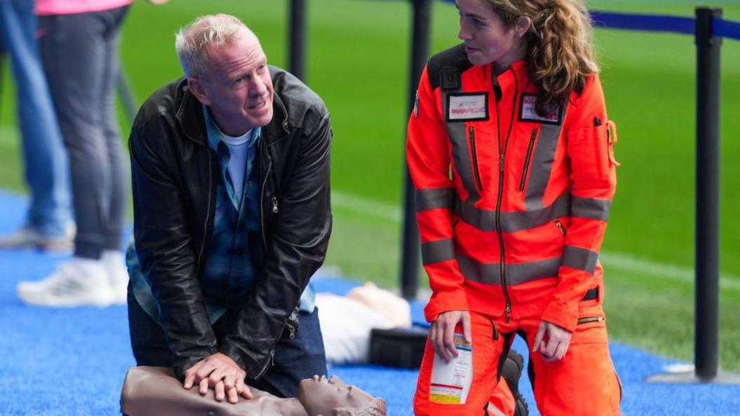 Fatboy Slim being taught how to do CPR at Amex Stadium in Falmer 