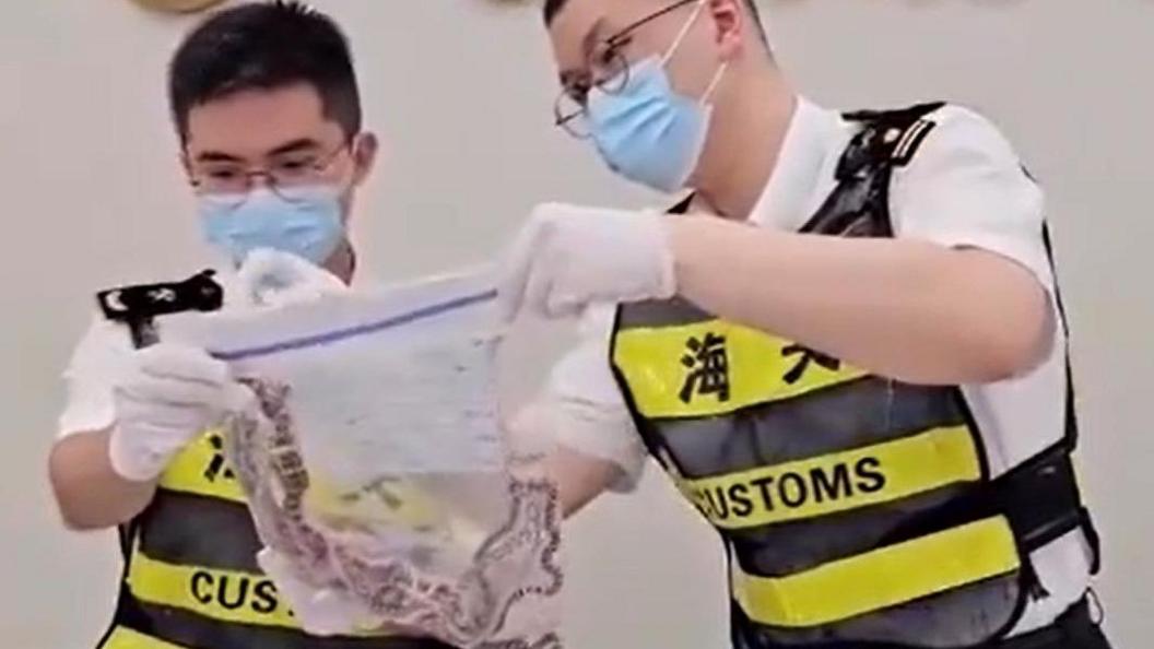 Two men hold up a bag of pink and red/black snakes. 