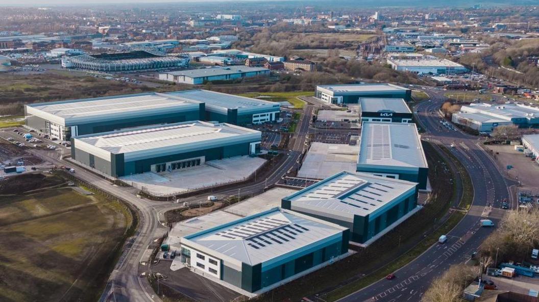 An aerial shot of eight large modern warehouses on the edge of a city