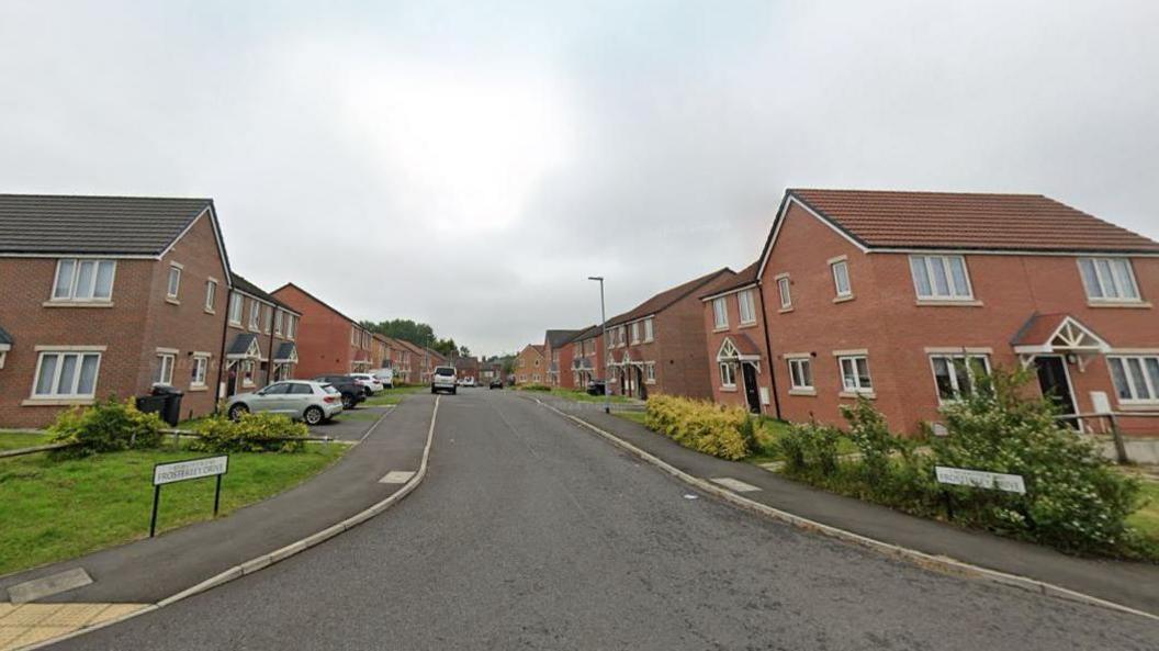 Street view of a road running between two lines on two-storey red brick houses.