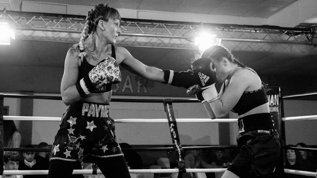 Lucy Payne  during a boxing match with another woman. The two women appear in a black and white filter while fighting in a ring.