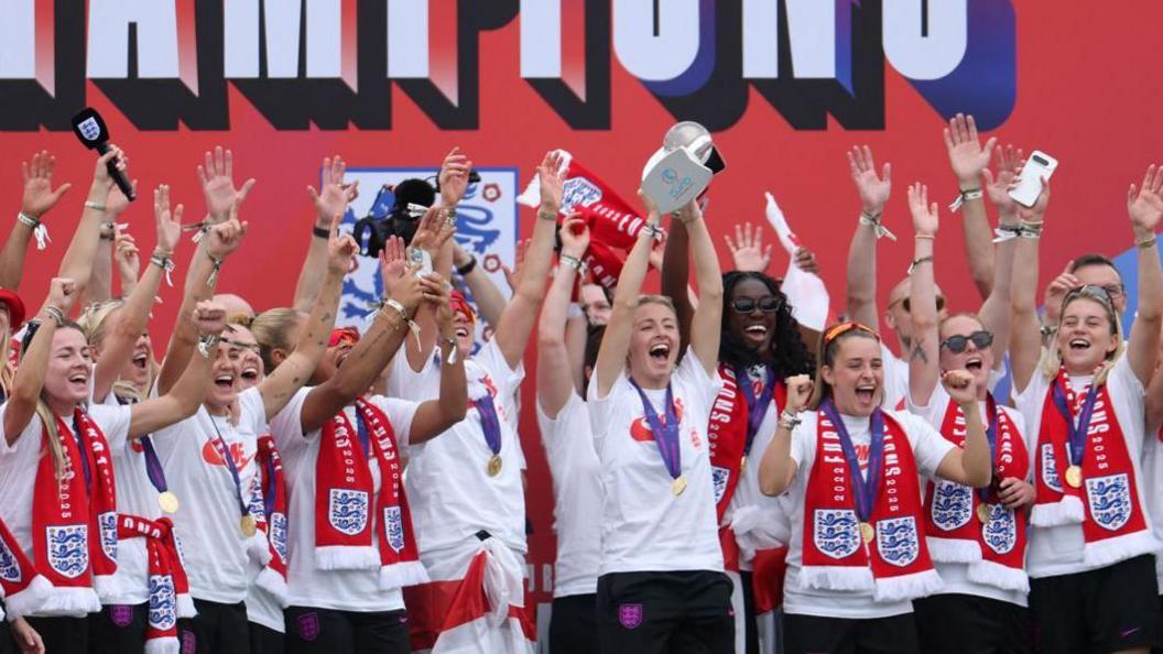 Leah Williamson lifts the Euro 2025 trophy on the stage following England's bus parade in London