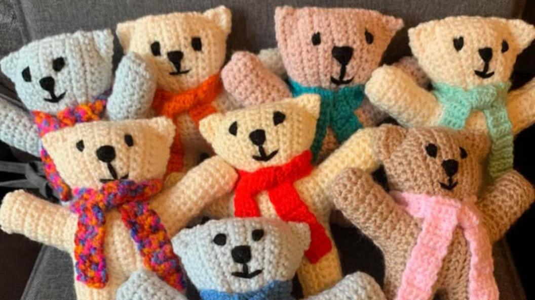 Eight bears clad in scarves, made with yellow, pink, blue and beige wool