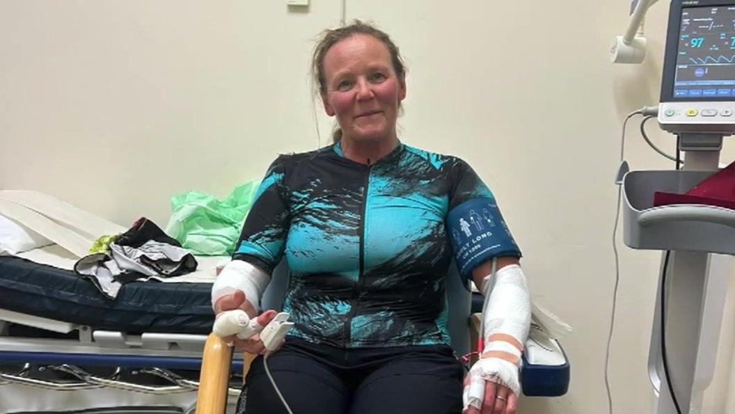 Beckie Hamilton in cycling gear sat on a hospital chair with bandages on and monitors around her.