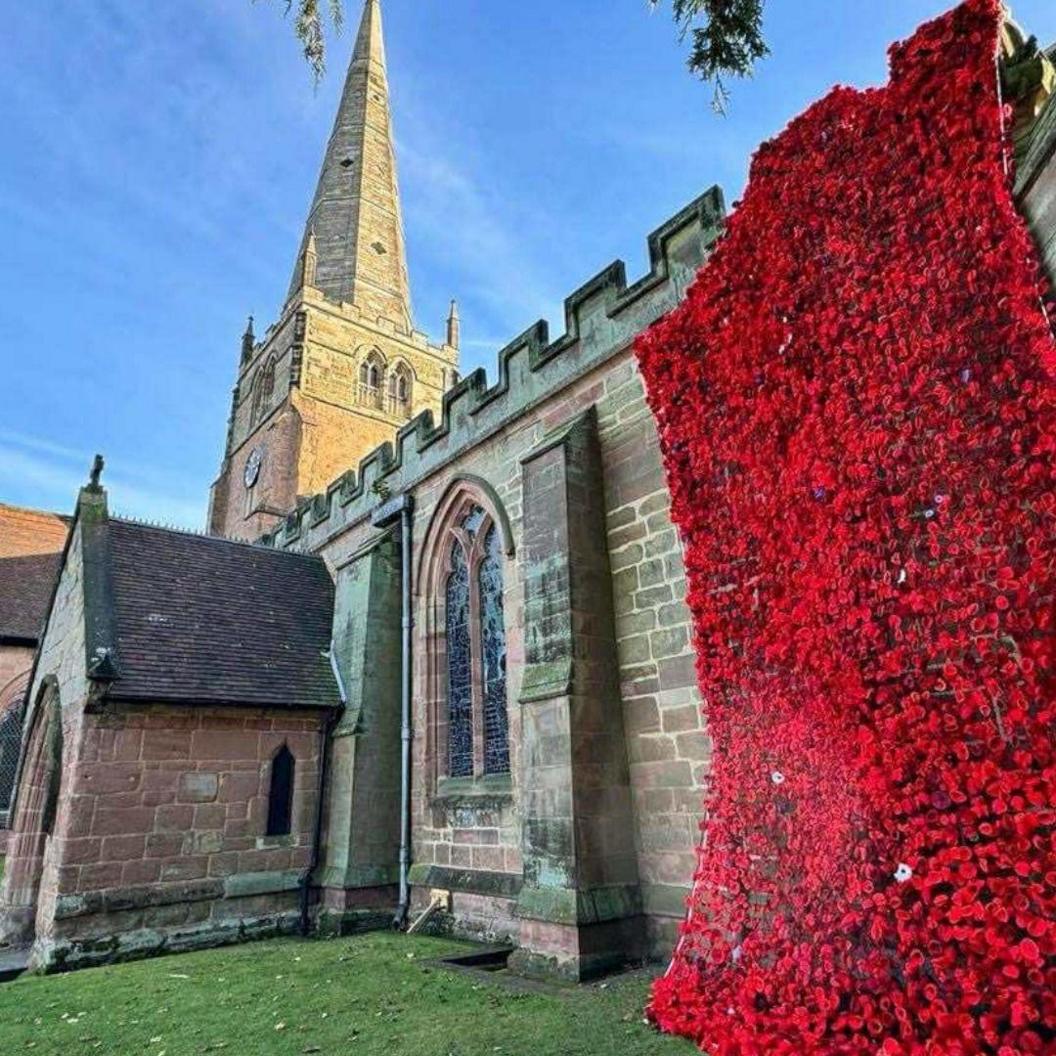 8,000 knitted poppies on the outside wall of a church, hanging in a rectangle shape.