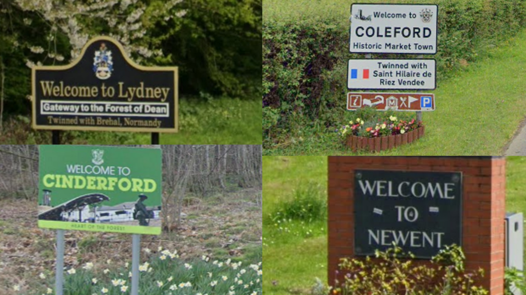 Four road signs of different sizes and styles - some traditional metal signs, another written on brick, welcome drivers to the four market towns in the Forest of Dean of Lydney, Coleford, Cinderford and Newent.