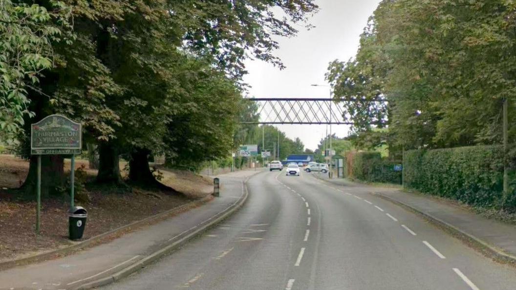 A street view of Melton Road in Thurmaston, showing a sign for Thurmaston Village on the left of the image.