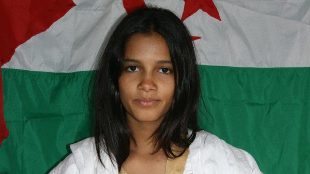 Fatimatu Bachir aged 13, with long black hair and a white dress in front of a Western Sahara flag