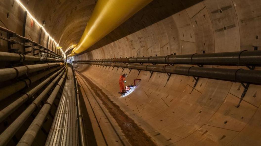 A man in a white hard hat and orange overalls working in a large tunnel