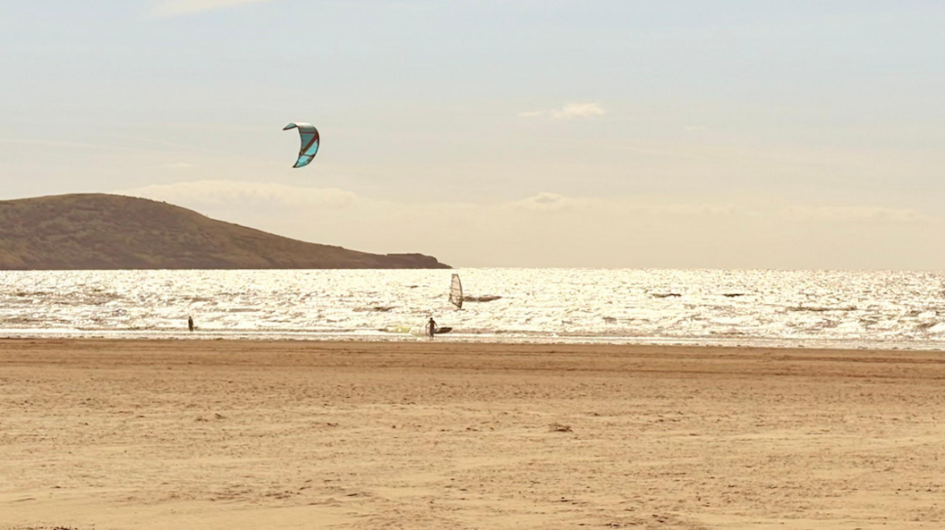 Two kite surfers on the beach in Weston-super-Mare. The sea is reflecting the sun brightly and the sand is flat.
