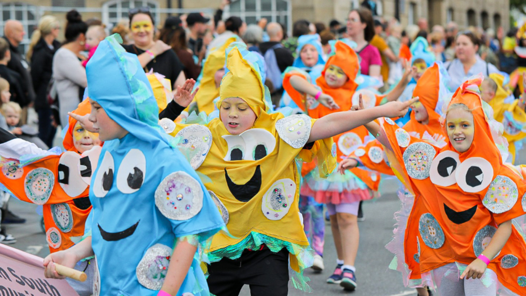 Children dressed as colourful stars dance on the high street.