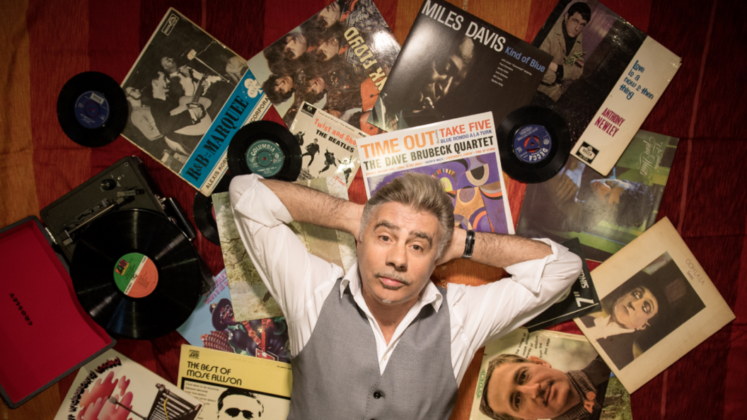 Glen Matlock lying on a pile of spread out records, including albums by Miles Davis, the Dave Brubeck Quartet, The Beatles and Anthony Newley