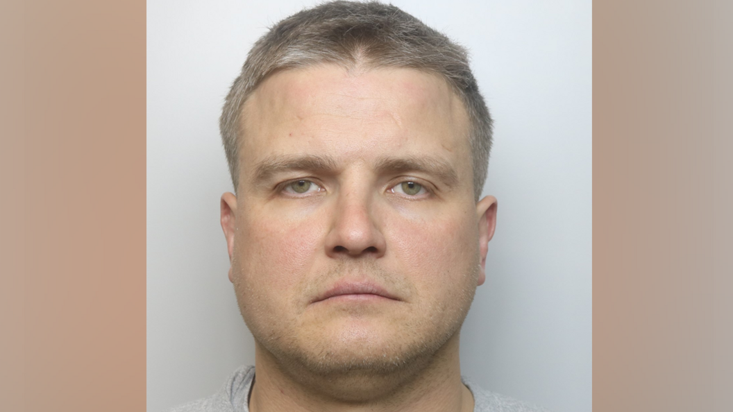 A police mugshot of Tadas Diksas, he is looking straight at the camera, has short fair hair, stubble on his face. 
