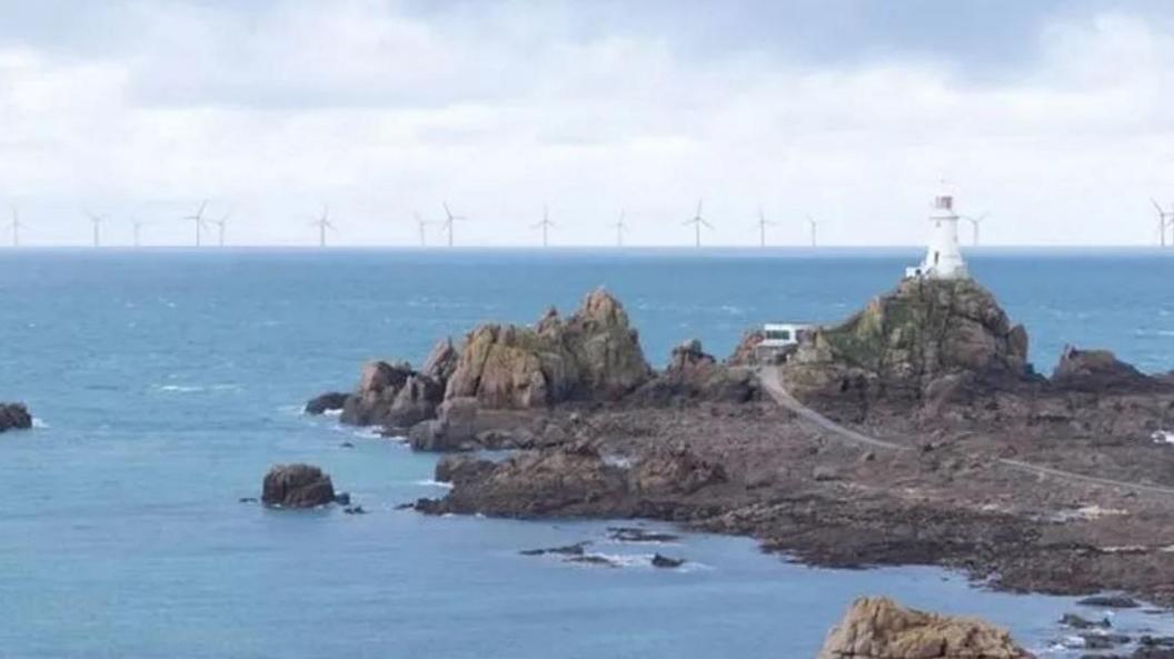 A mock-up image of a wind farm from the Government of Jersey, showing a lighthouse on an island peninsula, with a number of wind turbines at sea on the horizon