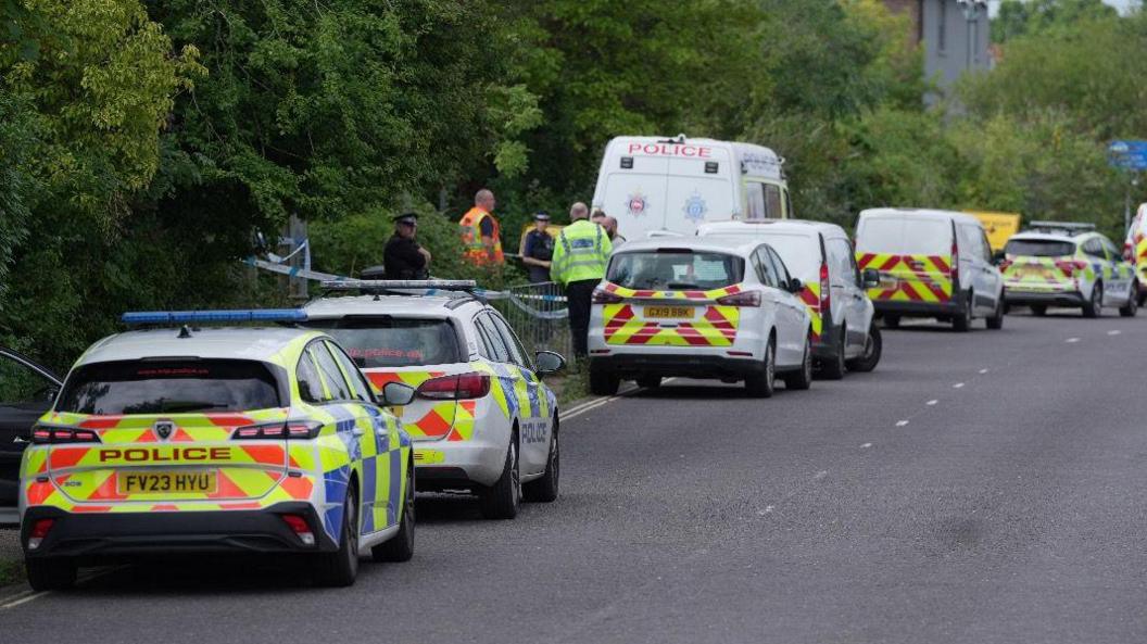 Four police cars and three police vans parked on the side of a road