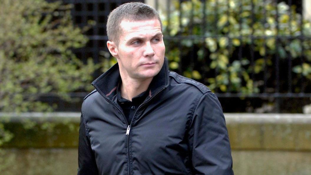 A man with short cropped hair and a serious expression photographed outside a court building. He is looking off to his left.
