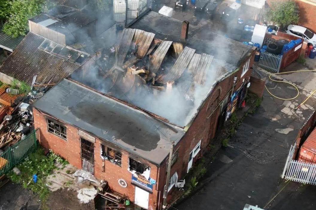 An aerial image of a two-story commercial building with a fire-damaged roof. Smoke is rising from the roof.