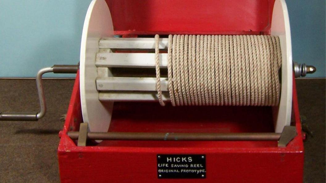 A red box contains a white reel with white rope wrapped around it and a handle to the side to wind it in.