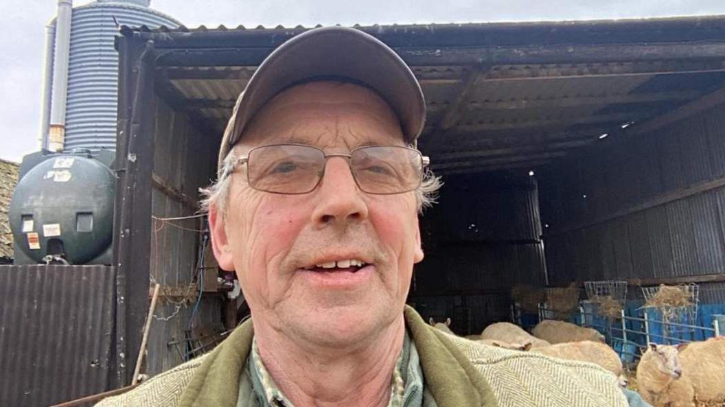 Farmer man with glasses taking a selfie in front of sheep on his farm