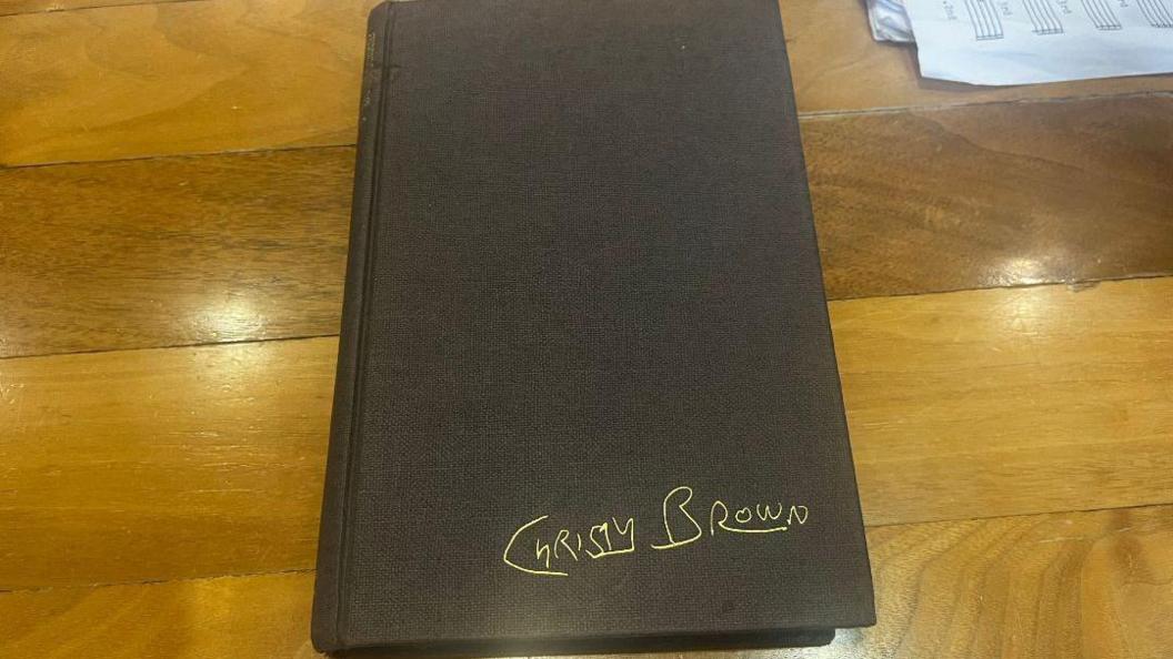 A closed black book, in good condition, with the words Christy Brown in gold on the bottom right hand corner